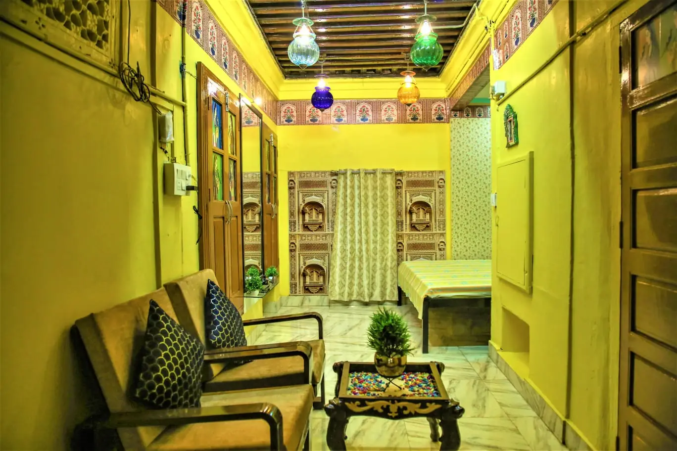 Palatial Deluxe Room with yellow lime plaster walls, painted floral borders, teak beam ceiling with coloured glass lanterns and marble floors, Jodhpur