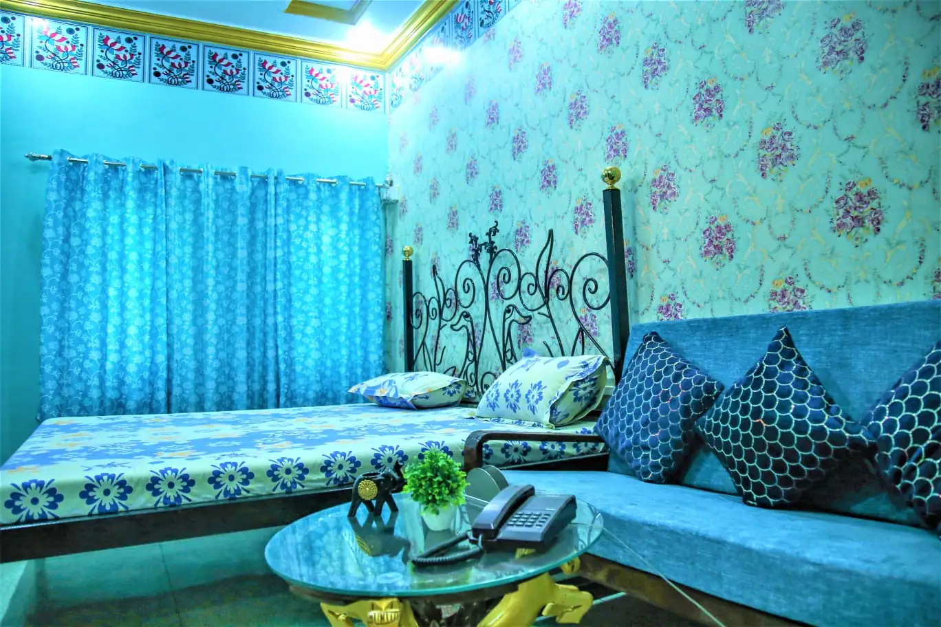 Imperial Deluxe Room, Saji Sanwri Heritage Inn Haveli Jodhpur Imperial Deluxe Room at Saji Sanwri Heritage Inn Haveli with blue floral wallpaper, wrought iron bed, blue sofa and glass coffee table in the blue city of Jodhpur
