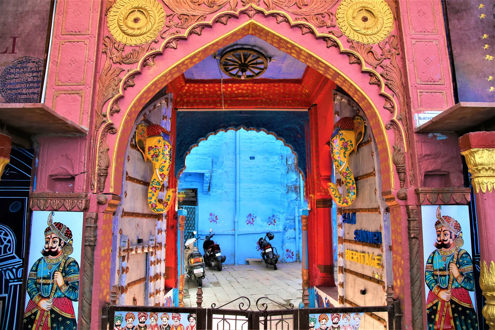 Arched heritage gateway of the haveli painted pink and gold opening onto a blue city lane