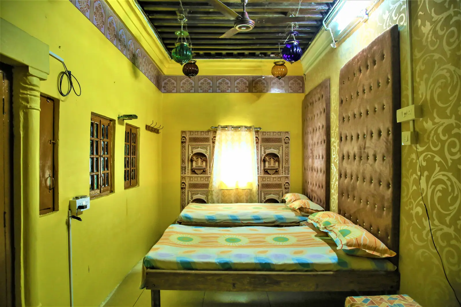 Twin queen beds under coloured glass lanterns in the Majestic Deluxe Room of the haveli